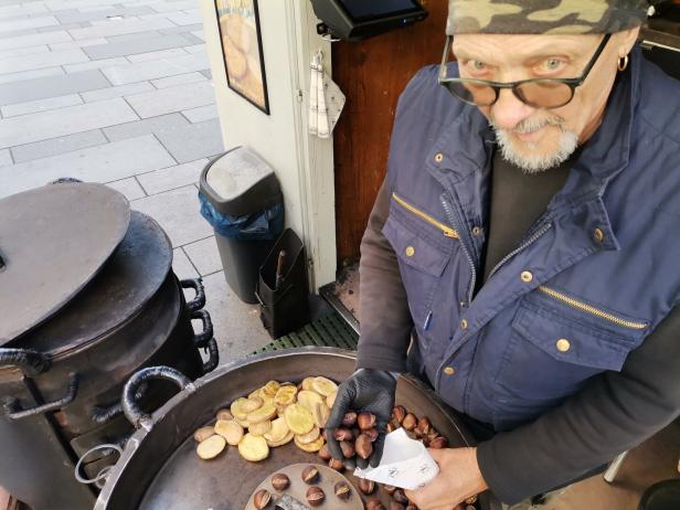 Ein Mann nimmt heiße Maroni aus dem Maroniofen.