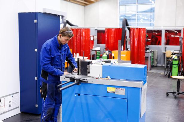 Junger Metalltechniker arbeitet konzentriert an einer blauen Maschine in einer Werkhalle.