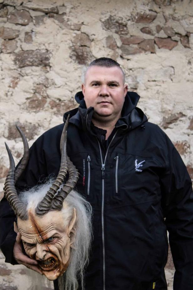 Mann in schwarzer Jacke mit einer Perchtenmaske in der Hand