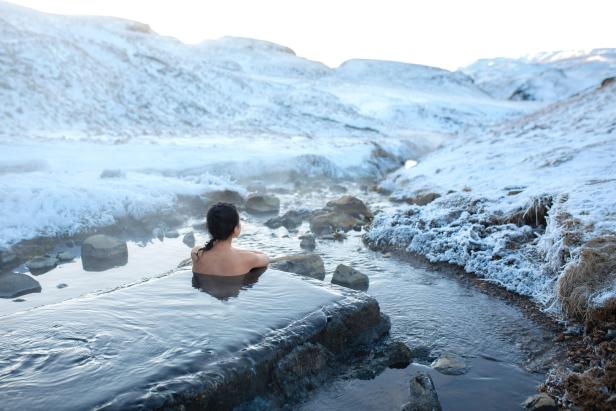 Eine Person entspannt in einer heißen Quelle, umgeben von schneebedeckter Landschaft und Bergen.