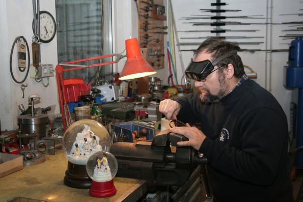 Ein Mann mit Schutzbrille arbeitet an einem Werkstück im Schraubstock, neben ihm Schneekugeln.