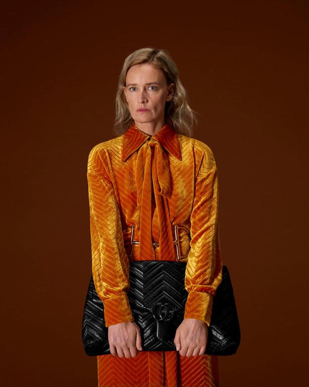 Eine Frau in einer orangen Bluse mit einer schwarzen Tasche in der Hand