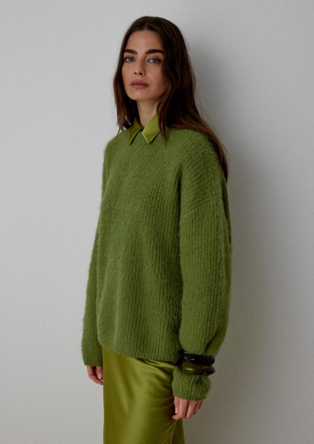 Eine braunhaarige Frau in grünem Pulli und grünem Rock.