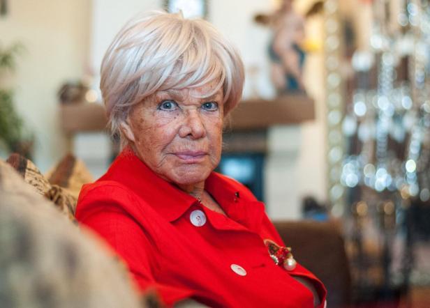 Ingrid Bergen mit blondem Haar trägt eine rote Jacke und blickt in die Kamera.