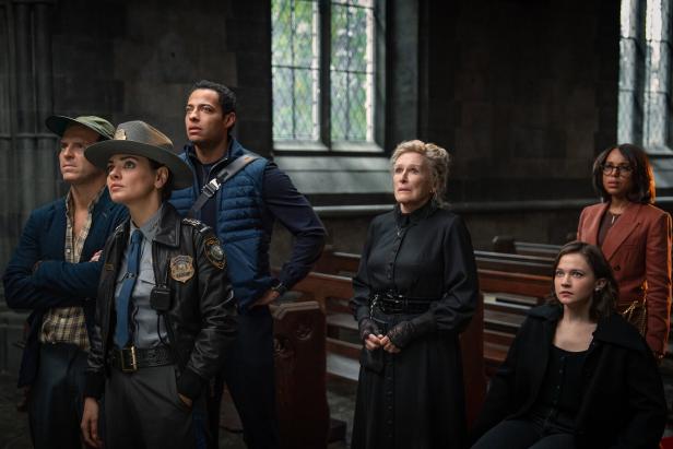 Eine Gruppe von Personen, darunter eine Polizistin und Glenn Close, blickt in einem Raum mit Kirchenbänken nach oben.