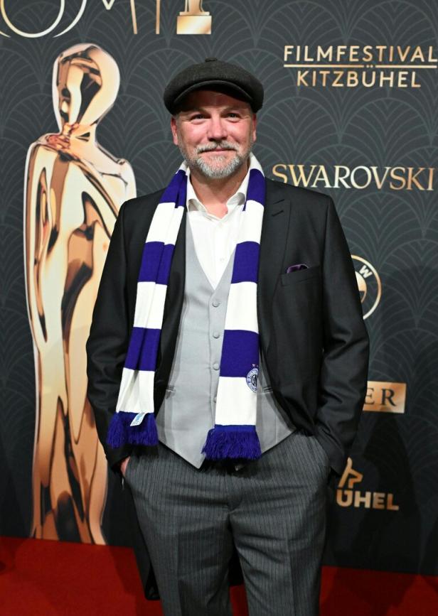 Thomas Stipsits mit Schal steht vor dem Hintergrund des Filmfestivals Kitzbühel.