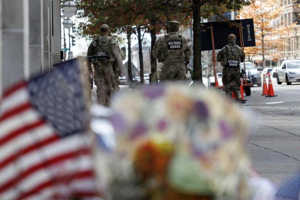Nationalgardisten patrouillieren auf einer Straße, im Vordergrund eine US-Flagge und Blumen.