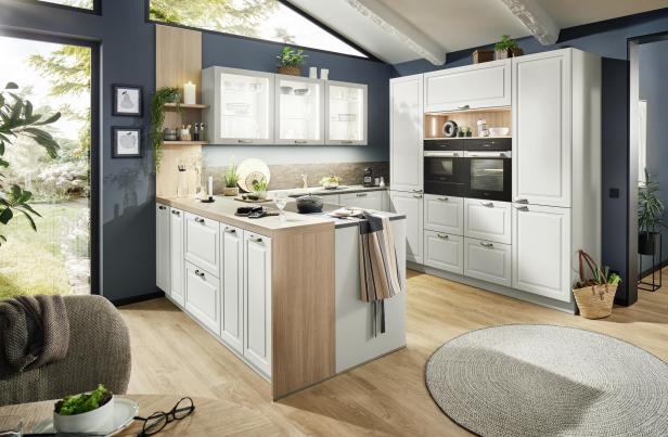 Moderne Küche mit weißen Schränken, Holzarbeitsflächen, Pflanzen, großen Fenstern und viel Tageslicht.