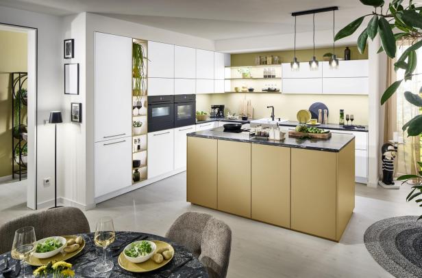 Moderne Küche mit goldener Kochinsel, weißen Schränken, Esstisch mit zwei Gedecken und viel Grünpflanzen.