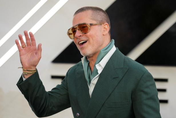 Brad Pitt mit Sonnenbrille und grünem Anzug winkt in die Kamera.