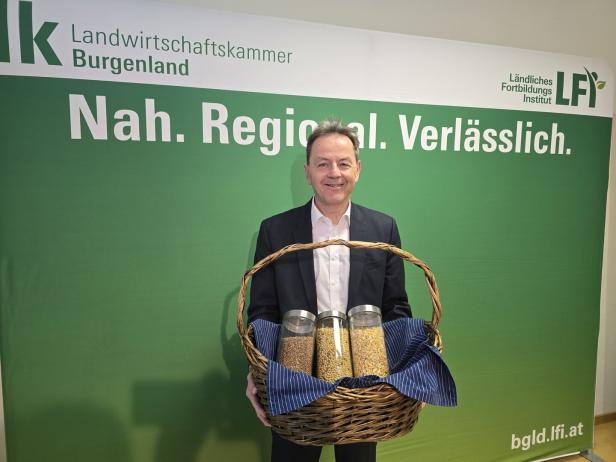 Ein Mann im Anzug hält einen Korb mit drei Gläsern voller Getreide vor einem grünen Hintergrund mit Werbeaufschrift.