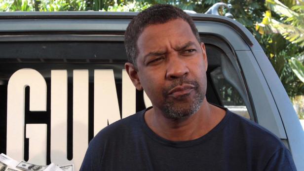 Denzel Washington mit ernstem Blick vor einem Auto mit der Aufschrift „GUNS“ und Bargeld.