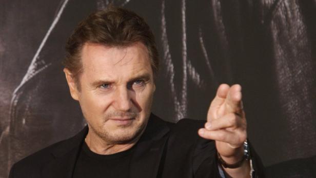 Liam Neeson gestikuliert vor einem dunklen Hintergrund.