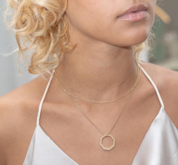 Nahaufnahme einer blonden Frau in einem weißen Kleid mit einer goldenen Halskette.