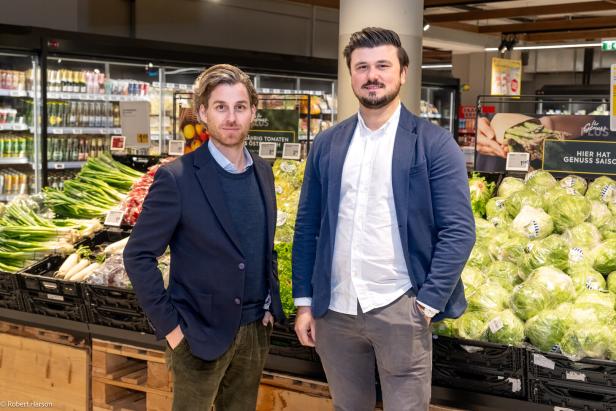 Zwei Männer stehen vor einem Gemüseregal im Supermarkt.