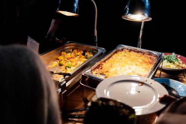 Zwei Warmhaltebehälter mit Gemüse und überbackenem Auflauf, daneben ein leerer Teller und eine Schüssel Salat.
