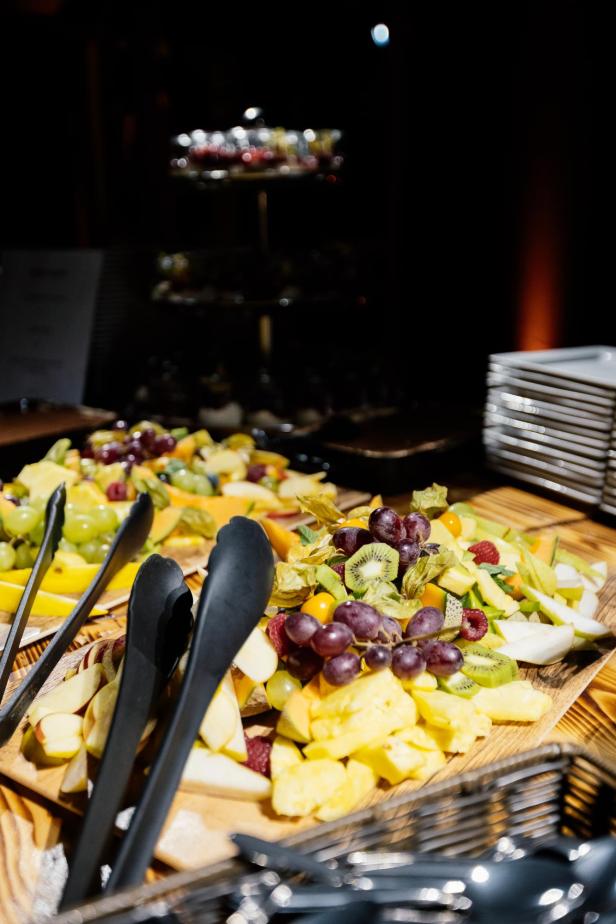Verschiedene geschnittene Früchte wie Trauben, Kiwi, Ananas und Äpfel liegen auf Holzplatten mit Zangen daneben.