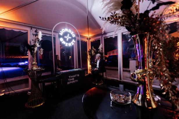 Ein festlich dekorierter Raum mit goldenen Vasen, einem beleuchteten „Nordic Spirit“-Schild und zwei Personen an einem Tresen.