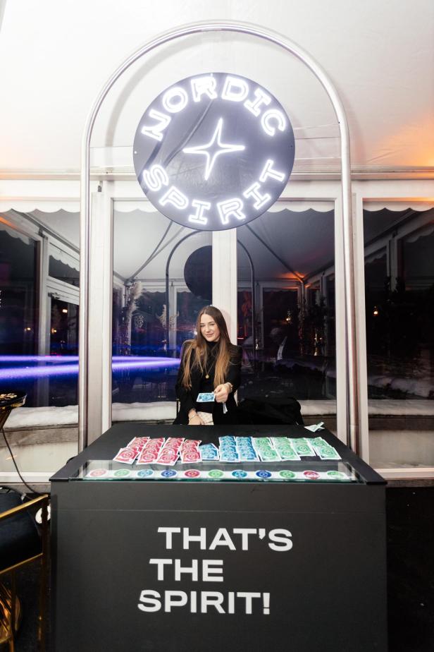 Eine Frau steht hinter einem Tresen mit bunten Päckchen und hält eines davon in der Hand, darüber leuchtet ein Nordic Spirit Schild.