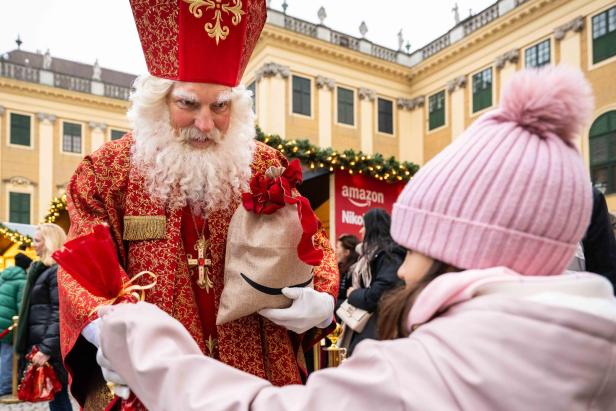 Nikolaus in rotem Gewand überreicht einem Kind ein Geschenk am Christkindlmarkt.