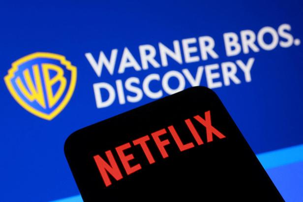 Das Netflix-Logo auf einem Smartphone ist vor dem Warner Bros. Discovery-Logo auf einem Bildschirm zu sehen.