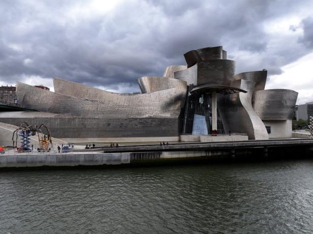 A drone view shows people walking past the Guggenheim Museum, alongside the River Nervion, in Bilbao
