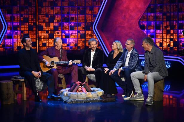 mehrere moderatoern einer mit gitarre an einem plastiklagerfeuer