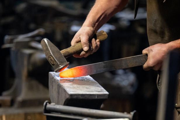 Eine Person bearbeitet ein glühendes Metallstück mit einem Hammer auf einem Amboss.