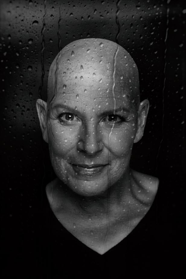 Eine Frau mit kurzem Haar blickt ernst in die Kamera, im Hintergrund sind Wassertropfen auf einer Scheibe zu sehen.