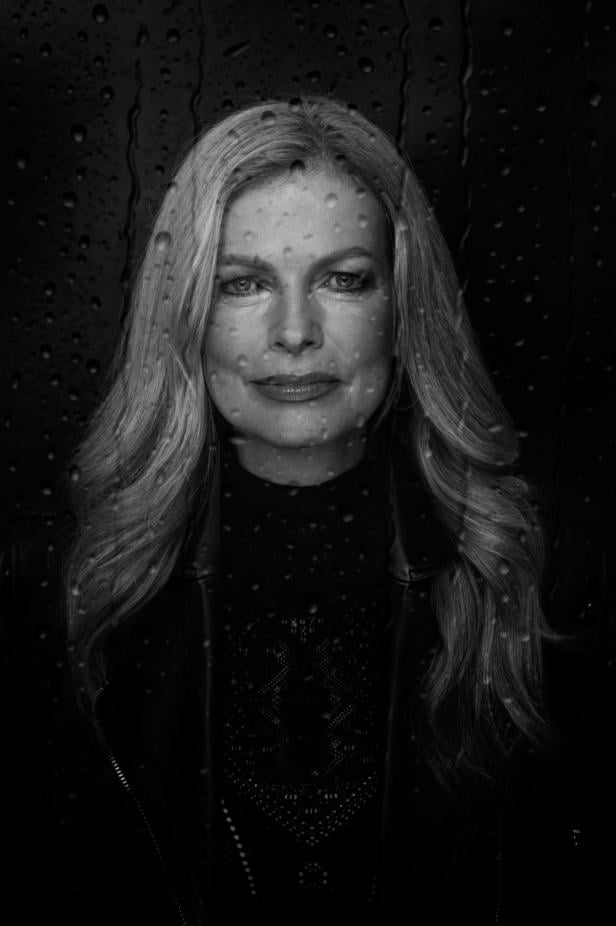 Eine Frau mit kurzem Haar blickt ernst in die Kamera, im Hintergrund sind Wassertropfen auf einer Scheibe zu sehen.