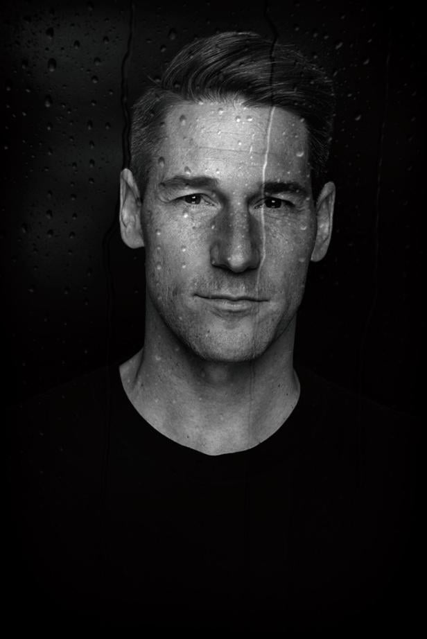 Eine Frau mit kurzem Haar blickt ernst in die Kamera, im Hintergrund sind Wassertropfen auf einer Scheibe zu sehen.