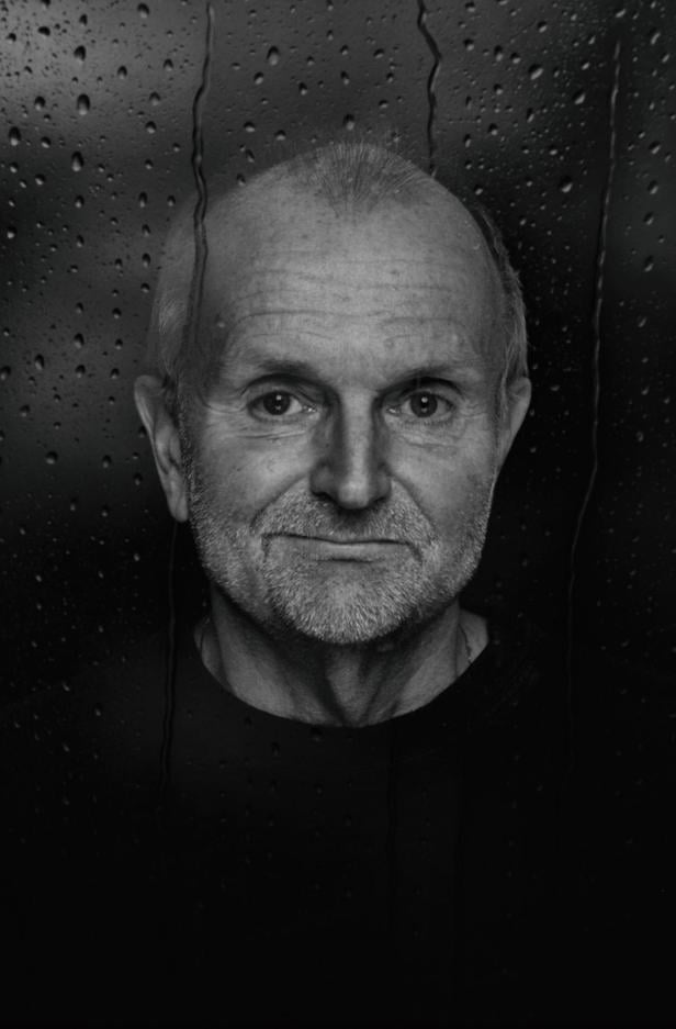 Eine Frau mit kurzem Haar blickt ernst in die Kamera, im Hintergrund sind Wassertropfen auf einer Scheibe zu sehen.