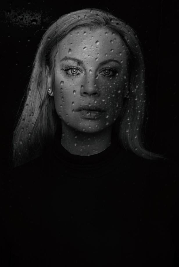 Eine Frau mit kurzem Haar blickt ernst in die Kamera, im Hintergrund sind Wassertropfen auf einer Scheibe zu sehen.