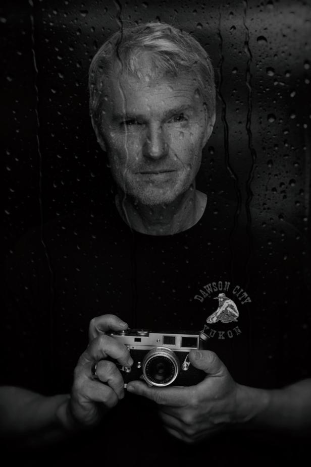 Eine Frau mit kurzem Haar blickt ernst in die Kamera, im Hintergrund sind Wassertropfen auf einer Scheibe zu sehen.