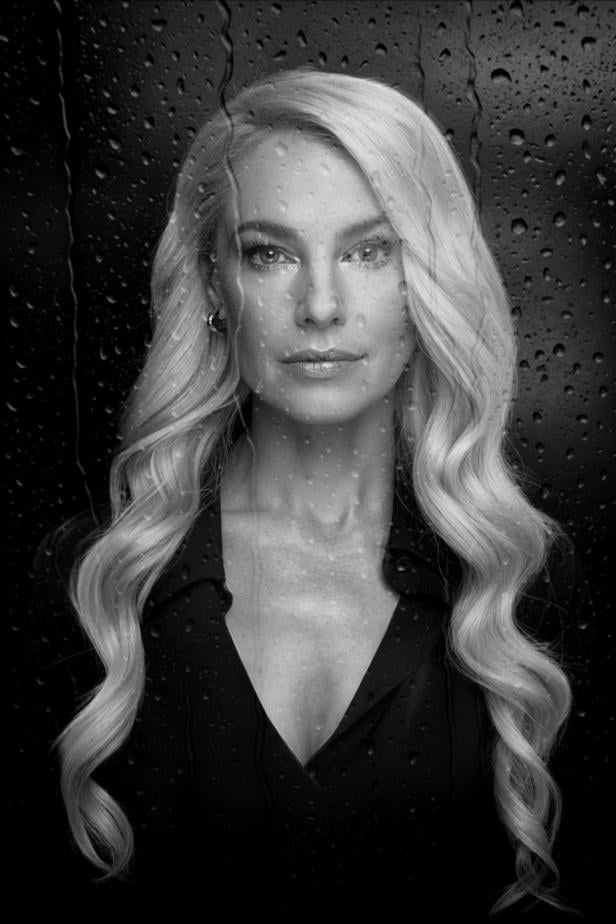 Eine Frau mit kurzem Haar blickt ernst in die Kamera, im Hintergrund sind Wassertropfen auf einer Scheibe zu sehen.