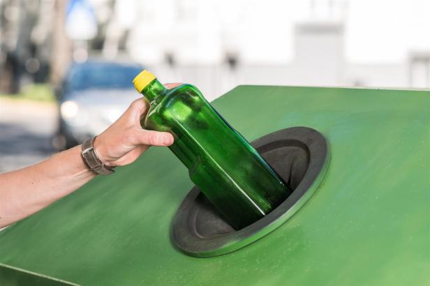 Eine männliche Hand wirft eine leere Ölflasche in einen Glascontainer.