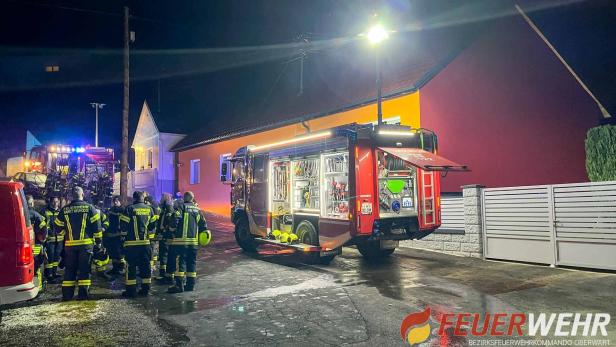 Mehrere Feuerwehrleute stehen nachts vor einem beleuchteten Einsatzfahrzeug neben einem Wohnhaus.
