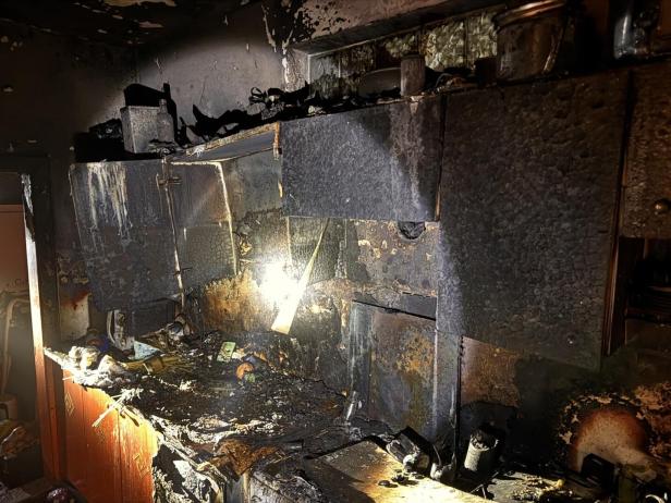Verkohlte und stark beschädigte Küchenschränke und Arbeitsfläche nach einem Brand, überall Ruß und Brandschäden.