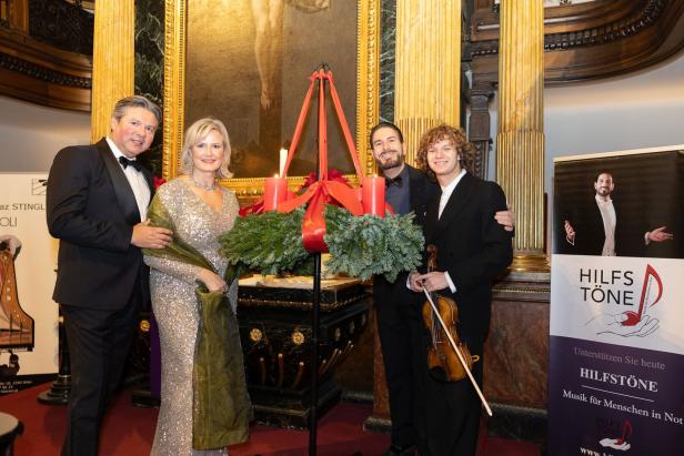 Festlich gekleidete Personen posieren neben einem Adventskranz und einem "Hilfstöne"-Plakat.