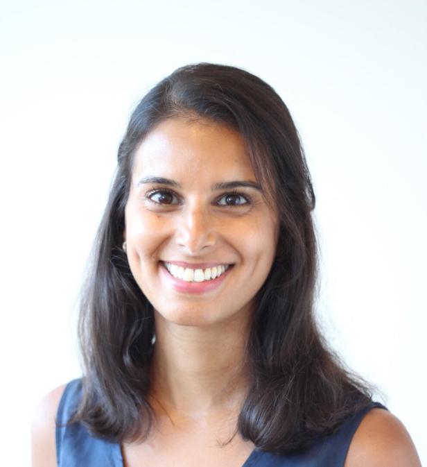 Junge Frau mit schulterlangem dunklem Haar lächelt freundlich vor hellem Hintergrund.