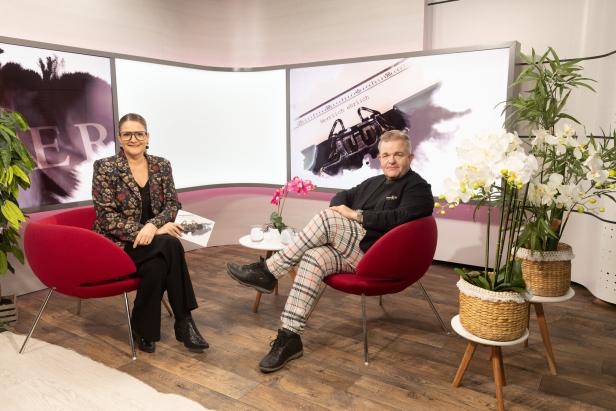 Zwei Personen sitzen in roten Sesseln in einem modern eingerichteten Studio mit Pflanzen und Orchideen.