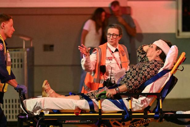 Eine verletzte Frau mit Kopfverband liegt auf einer Trage, während Rettungskräfte sie betreuen.