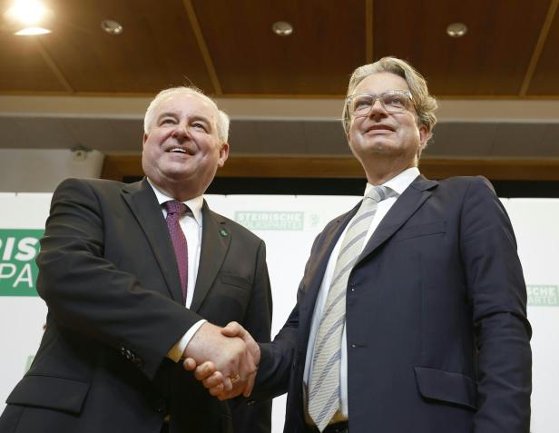 Zwei Männer im Anzug geben sich vor einem Schild mit der Aufschrift „Steirische Volkspartei“ die Hand.