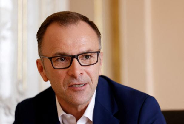 Ein Mann mit Brille und dunklem Sakko sitzt in einem hellen Raum und schaut leicht zur Seite.