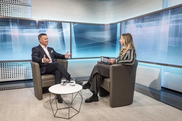 Ein Mann im Anzug und eine Frau führen ein Interview in einem Fernsehstudio.