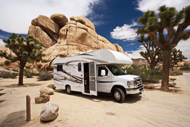 Ein Wohnmobil steht auf sandigem Boden zwischen Felsen und Bäumen im Joshua Tree National Park in Kalifornien.