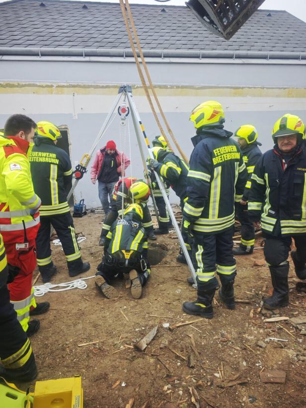 Mehrere Feuerwehrleute retten mit Spezialausrüstung eine Person aus einem Schacht auf einer Baustelle.