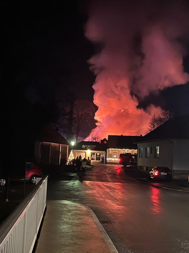 Große Rauch- und Feuersäule steigt nachts hinter Häusern auf, Menschen und Autos sind auf der Straße zu sehen.