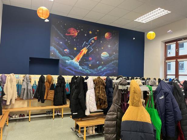 Mehrere Winterjacken hängen an Haken in einem Raum mit einer bunten Weltraumraketen-Malerei an der Wand.