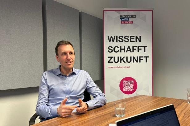 Mann im Gespräch an einem Tisch, im Hintergrund Roll-up mit Schriftzug „Wissen schafft Zukunft“.